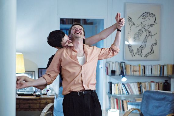 Zwei M&auml;nner tanzen und lachen in einem Wohnzimmer.