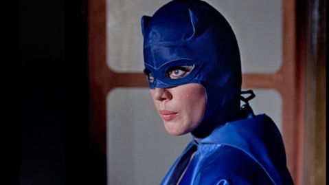 Eine Frau mit langen Wimpern in einer blauen Kostümmaske blickt zur Seite.