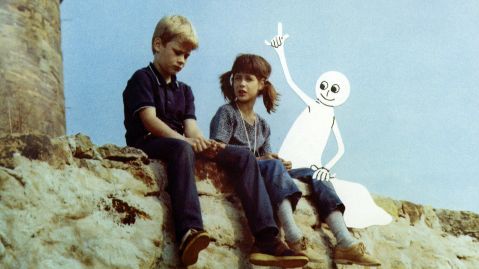 Zwei Kinder sitzen auf einer Mauer und unterhalten sich, daneben sitzt ein Zeichentrick-Gespenst und meldet sich.