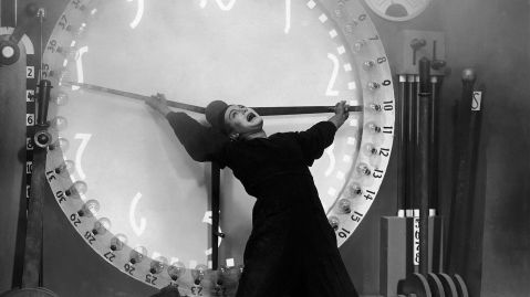 Ein Mann kniet vor einem technischen Ger&auml;t, das einer Uhr &auml;hnelt und h&auml;lt die Zeiger fest.
