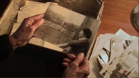 Hände halten ein historisches Schwarz-weiß-Foto, auf dem eine Frau aus einem Fenster schaut.