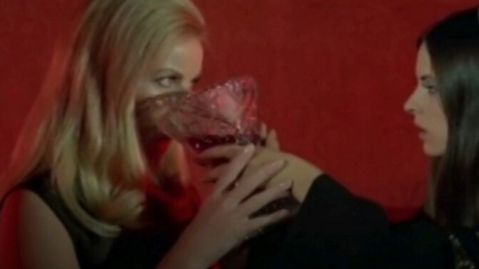 Eine blonde und dunkelhaarige Frauen trinken aus einem kelchartigen Glas, das sie gemeinsam halten.