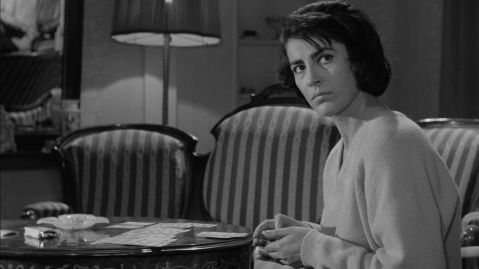 Eine Frau an einem Tisch  mit Spielkarten schaut mit ernstem Blick auf.