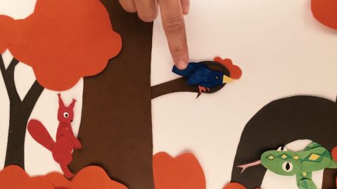 In einer Trickfilmszene, in der alle Elemente aus Pappe gelegt wurden, sitzen ein Eichhörnchen, ein Vogel und eine Schlange auf einem Baum.
