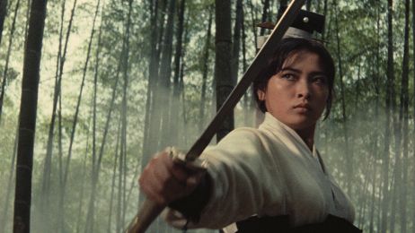 Eine Frau mit einem Stab schaut k&auml;mpferisch in die Ferne im Wald.