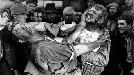 Zwei M&auml;nner in Schwarz-Wei&szlig; pr&uuml;geln sich vor Zuschauern, ihre Kleidung ist voller Blut.