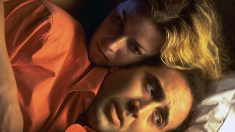 Ein Mann und eine Frau liegen im Bett, sie umarmt ihn von hinten.