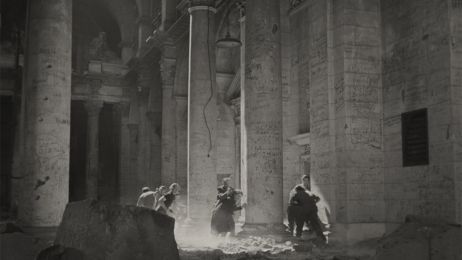 Eine Gruppe Menschen steht in einem antik aussehenden Geb&auml;ude mit S&auml;ulen.