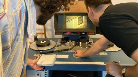 Zwei Männer von hinten schauen auf einen Bildschirm, auf dem ein Film mit einem Projektor abgespielt wird.