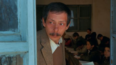 Ein Mann schaut ernst aus einem Fenster, hinter ihm sitzt eine Schulklasse.