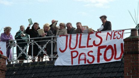 Menschen stehen auf einem Dach und halten ein Banner mit französischem Schriftzug nach unten.