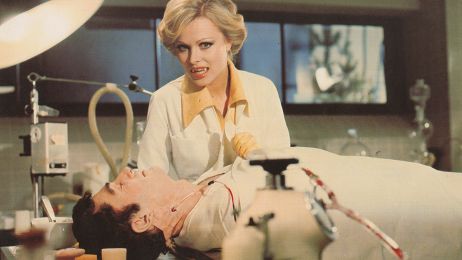 Eine Frau mit blonden Haaren und Vampirz&auml;hnen beugt sich &uuml;ber einen Mann in einem OP-Saal und faucht in die Kamera.