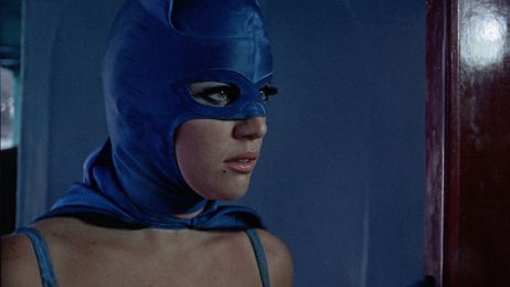 Eine Frau mit langen Wimpern in einer blauen Kostümmaske blickt zur Seite.