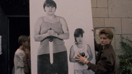 Eine Frau tr&auml;gt ein Plakat, auf der eine andere Frau mit einem Messer zu sehen ist