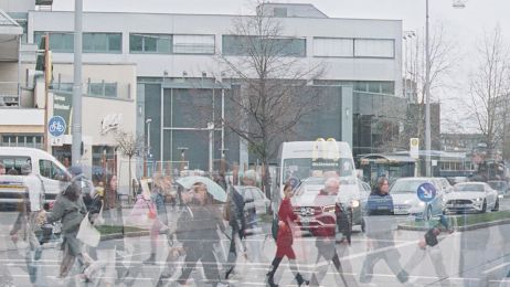 Menschen laufen in Unschärfe über eine Straße in Berlin unter einem grauen Himmel.