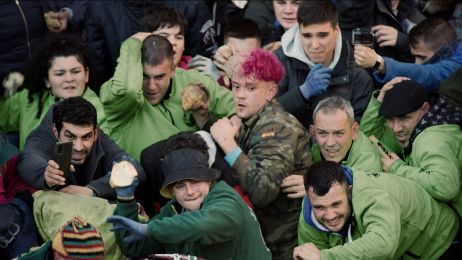 Eine Gruppe überwiegend dunkelhaariger Menschen steht auf einer Straße und versucht, sich gegen etwas zu verteidigen.