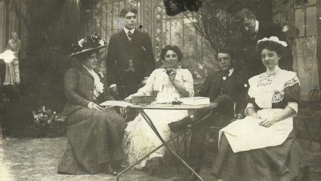 Sechs Mitglieder der Pariser Filmfirma Pathé Frères sitzen fröhlich draußen um einen Tisch.