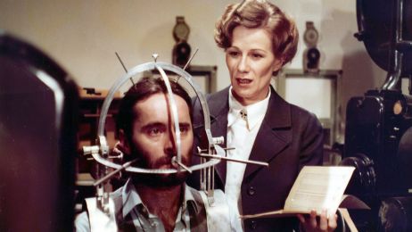 Neben einem Mann mit einem helmartigen Kopfaufsatz steht eine Frau mit einem Notizheft.