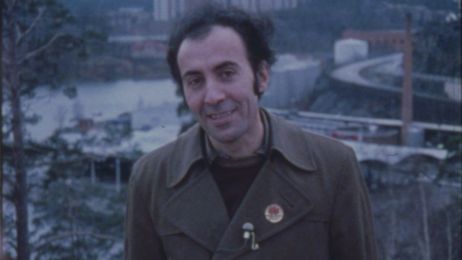 Iranischer Mann mit angestecktem Mikro an der Jacke l&auml;chelt in die Kamera vor einer Stadtansicht.