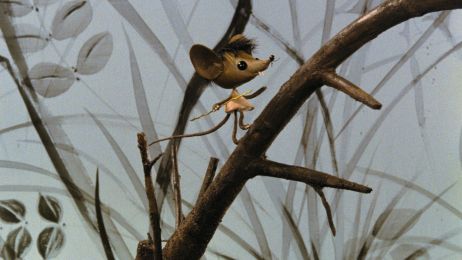 Ein Maus aus Holz l&auml;uft auf einem Zweig, im Hintergrund Gr&auml;ser und Bl&auml;tter.