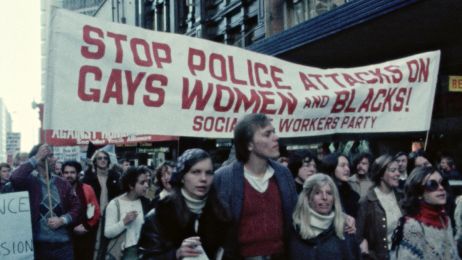Demonstrierende Menschen mit Plakaten gegen Rassismus und Sexismus laufen durch eine Stra&szlig;e.