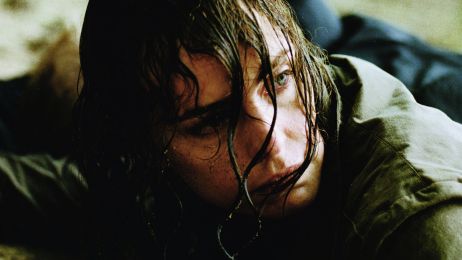 Eine nasse, schmutzige Frau liegt am Boden und schaut hoch.