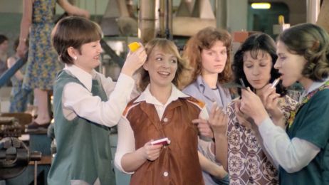 Eine Gruppe von jungen Frauen auf dem Arbeitsplatz. Sie machen sich zurecht (eine schminkt sich die Lippen, eine andere k&auml;mmt einer anderen die Haare), sie lachen.