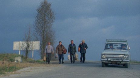 Vier Personen gehen auf einer Stra&szlig;e, ein Auto f&auml;hrt neben ihnen.