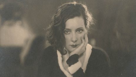 Eine junge Frau sitzt, den Kopf in die Hand gest&uuml;tzt. Mit ernstem Blick schaut sie direkt in die Kamera.