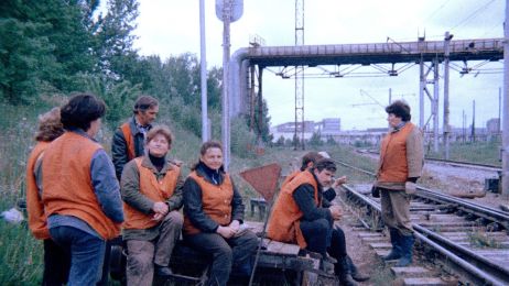 Eine Gruppe von Menschen in orangefarbenen Westen steht und sitzt am Rand eines Zuggleises.