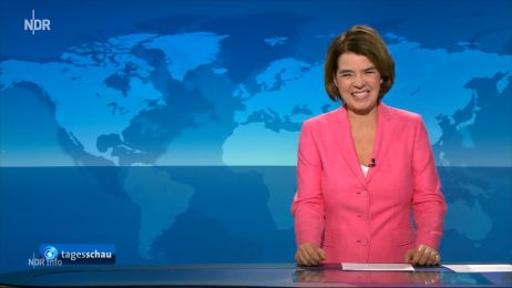 Nachrichtensprecherin im pinken Jackett l&auml;chelt im Tagesschau-Studio, vor blauer Weltkarte, H&auml;nde auf dem Tisch, Logos links unten im Bild.