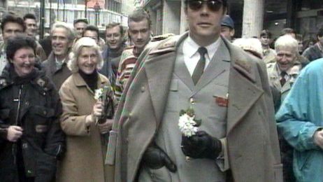 Ein Mann verkleidet als Tito, in Uniform mit Blumenstrau&szlig;, umgeben von Menschen.