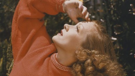Marlene Dietrich in einem roten Strickpullover schaut in den Himmel.