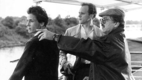 Schwarzwei&szlig;aufnahme von Regisseur Heinrich Breloer w&auml;hrend der Dreharbeiten auf einem Boot, wo er mit der Hand nach links zeigt, w&auml;hrend die beiden Schauspieler in dieselbe Richtung blicken.