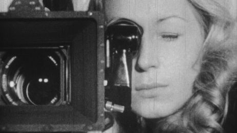 Schwarzwei&szlig;aufnahme einer Frau, die durch die Linse einer Filmkamera schaut.