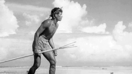 Schwarzwei&szlig;aufnahme eines Mannes der indigenen polynesischen Bev&ouml;lkerung von Bora Bora am Strand, mit einem Speer in der Hand.