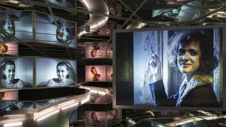 Ausstellungsraum mit beleuchteter Laufbahn und Filmprojektionen, Frauenportr&auml;ts in Farbe und Schwarz-Wei&szlig;, cineastische Atmosph&auml;re mit Spiegeln.